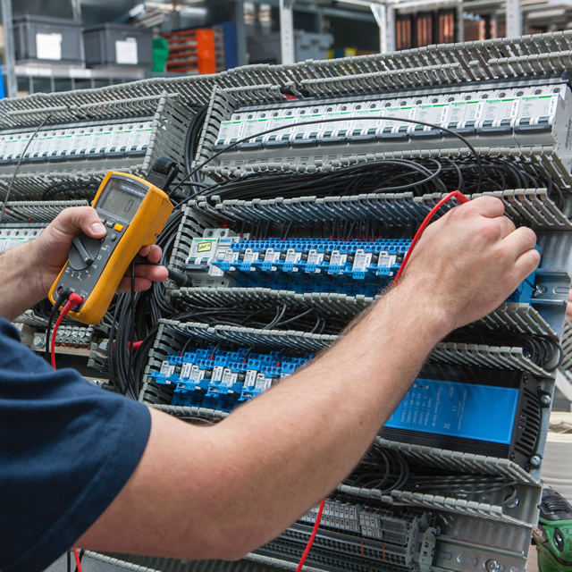 Technicus Siegers Technics meet bedrading en schakelingen in een verdeelbord voor bordenbouw, met gebruik van een multimeter voor precisiecontrole
